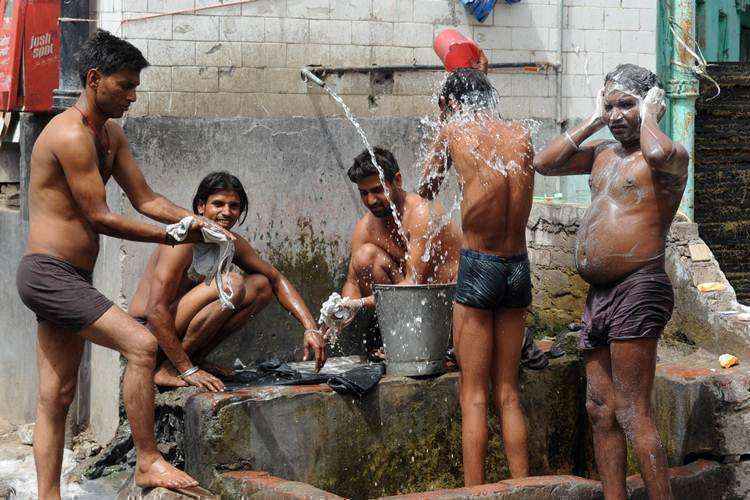 Homens indianos tomam banho com água de um cano à beira da estrada em Nova Deli