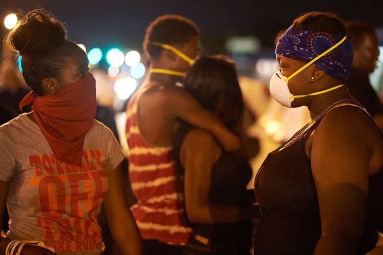 Duas mulheres conversam usando mascaras para se proteger das bombas de gás arremessadas pelos policiais