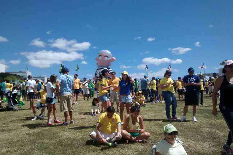 Manifestantes sentados no gramado em frente ao espelho d'água do Congresso Nacional