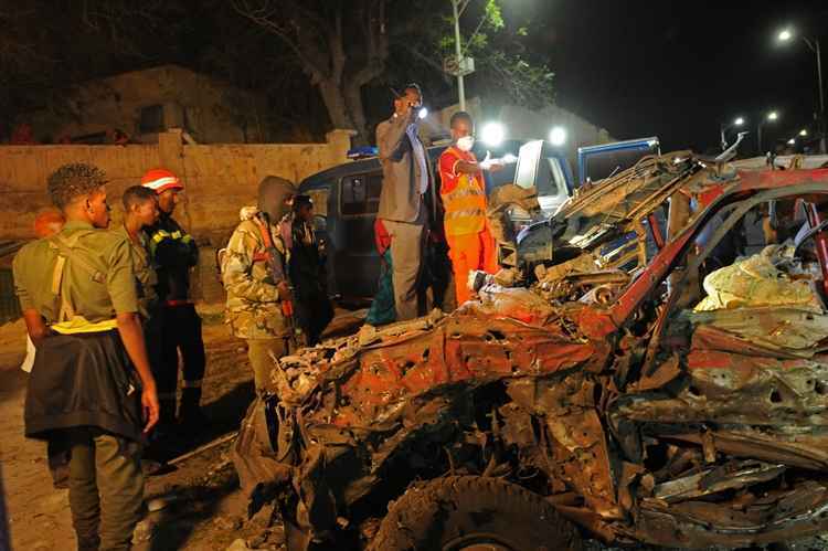 As pessoas olham para destroços do carro-bomba perto de um complexo habitacional