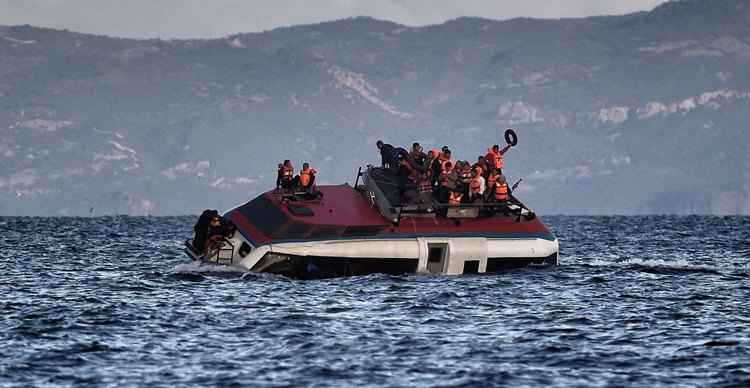 Refugiados esperam chegada de ajuda do resgate no topo do barco que naufraga