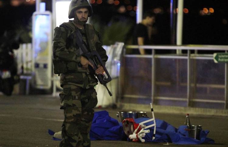 Soldado diante de corpos estirados no chão e cobertos com lençóis azuis, em Promenade des Anglais: depois da queima de fogos, a barbárie