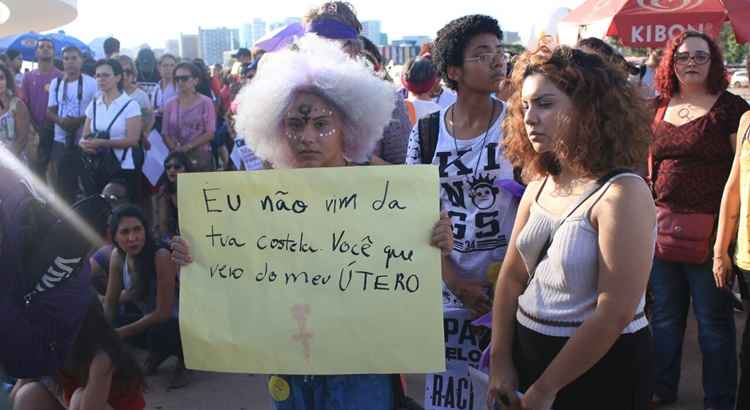 Mulher segura cartaz com dizeres: 