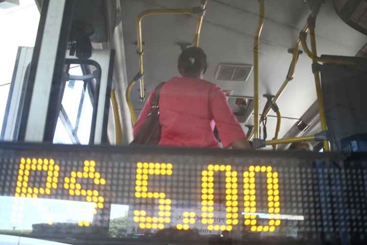 Mulher dentro de ônibus próxima a informação do valor da passagem, de cinco reais