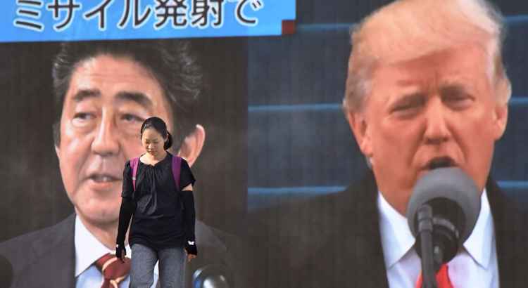 Mulher caminha em frente a tela onde é exibida foto do premiê Shinzo Abe  e do presidente Donald Trump: reação à Coreia do Norte