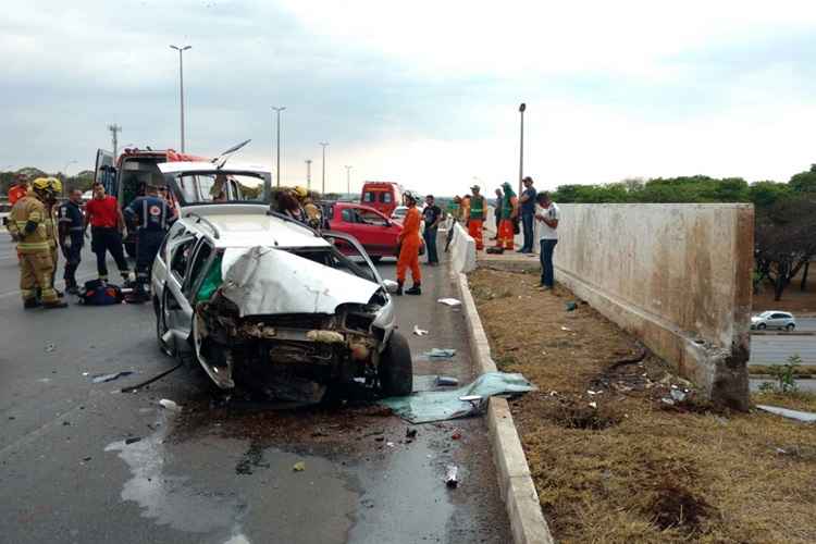 Carro branco com frente destruída ao lado de mureta em estrada