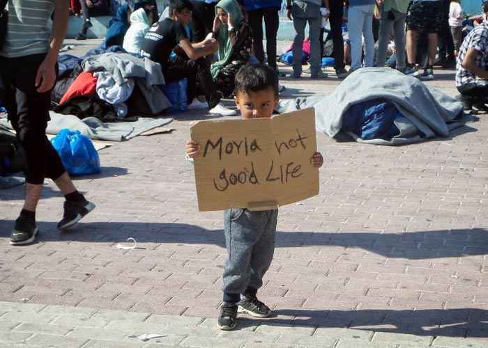 Criança segura cartaz dizendo que em Moria a vida não é boa