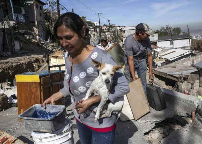 Pessoas carregam seus pertences e animais de estimação à medida que deixam suas casas depois que um deslizamento de terra causou danos no bairro de Lomas del Rubi, em Tijuana, no noroeste do México