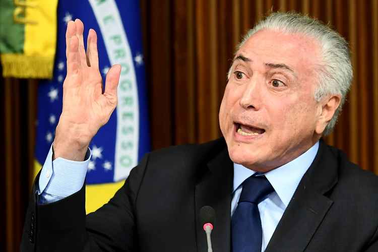 Michel Temer sentado com a mão direita levantada