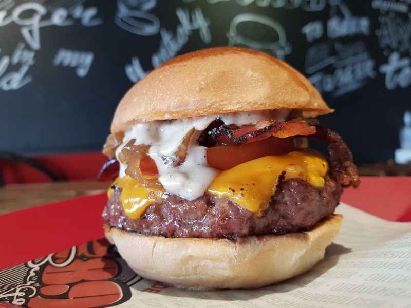 A foto é de um hambúrguer de carne, com molho branco e queijo amarelo.