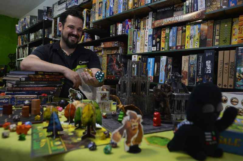 Um homem sorrindo na frente de um monte de jogos de tabuleiros coloridos.