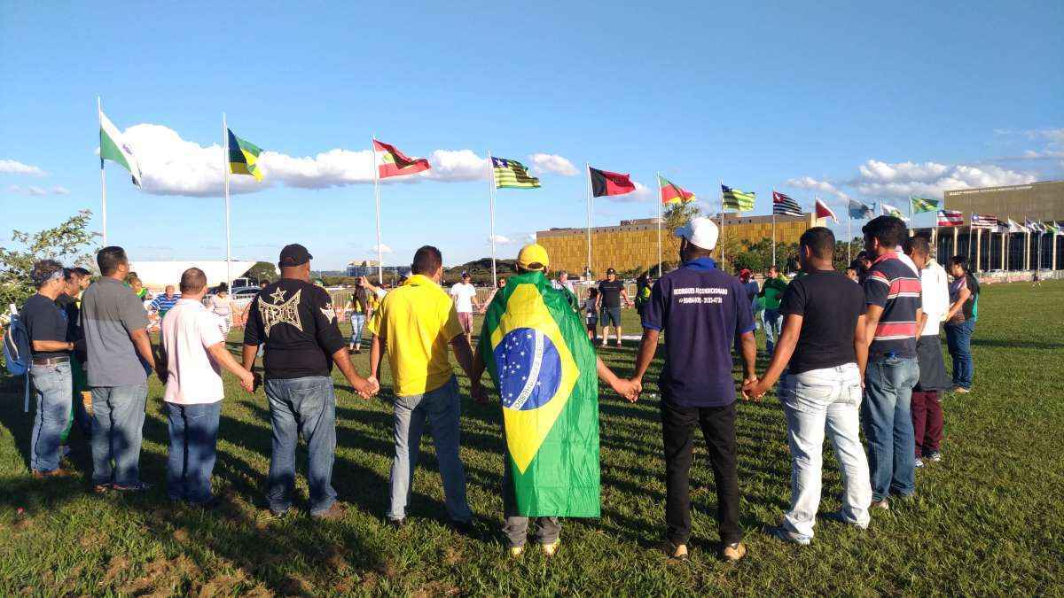 Manifestantes de mãos dadas em círculos, com bandeira do Brasil, na Esplanada dos Ministérios, em Brasília