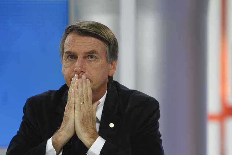 Bolsonaro sentado com as mãos em frente a boca