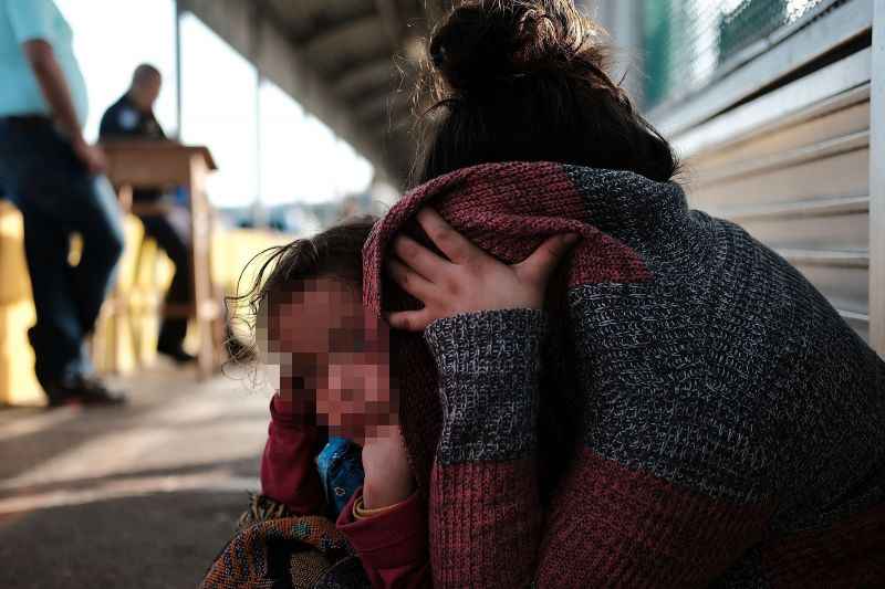 MUlher com criança no colo, cobrindo o rosto