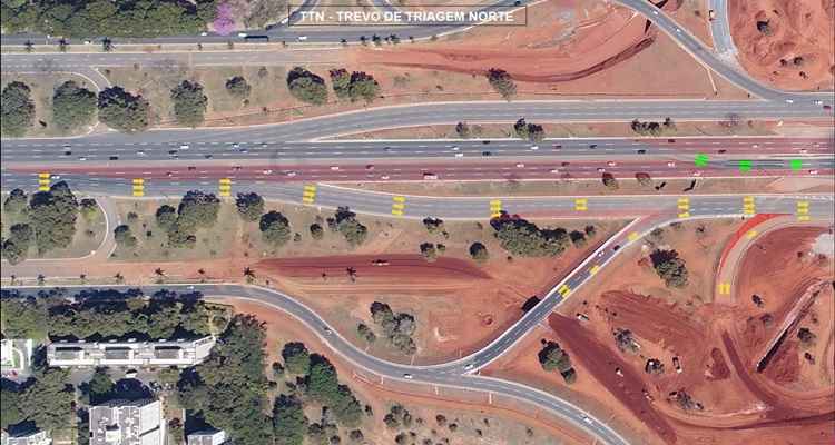 Foto aéreo de obras do trevo de triagem norte com desenhos indicativos em amarelo e vermelho sobre a imagem a respeito do trajeto dos carros na via.