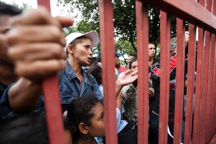 Venezuelanos em frente à portão vermelho em Boa Vista