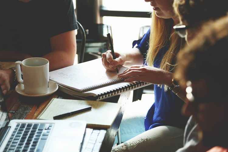 Foto de pessoas estudando, escrevendo e com notebooks pela mesa