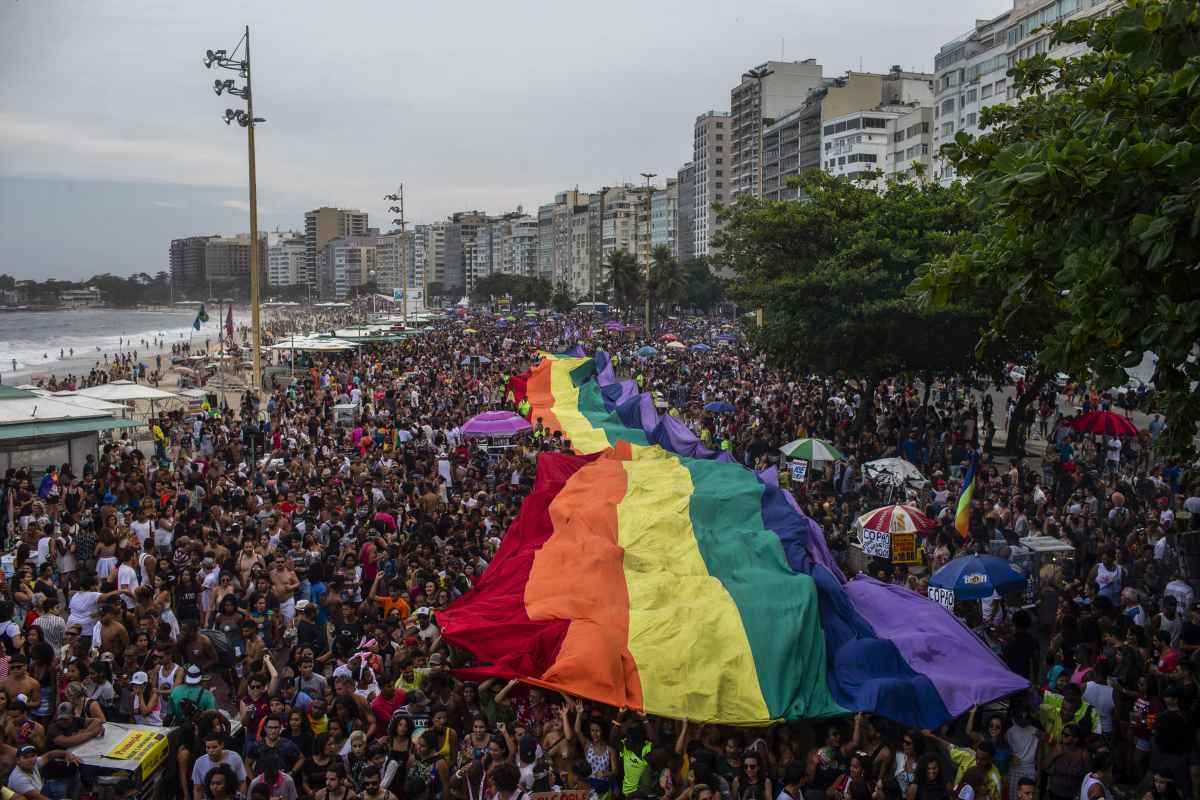 Multidão com bandeira LGBTI na Parada LGBTI, na orla da praia, Rio de Janeiro