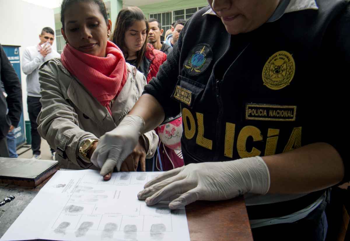 Um policial tira impressões digitais de um imigrante venezuelano enquanto solicita um visto de residência ou autorização de permanência temporária em uma instalação da Interpol em Lima em 29 de agosto de 2018.