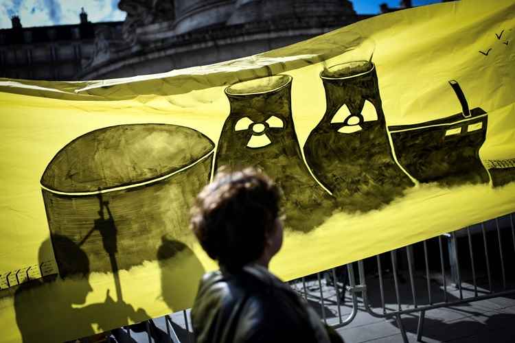 An environmental activist walks past a banner during a demonstration called by associations to mark the seventh anniversary of the Fukushima nuclear disaster in Japan, on March 11, 2018 in Paris. The deadly earthquake, tsunami and nuclear disaster seven years ago devastated Japan's northeastern coast and left around 18,500 people dead or missing. / AFP / STEPHANE DE SAKUTIN