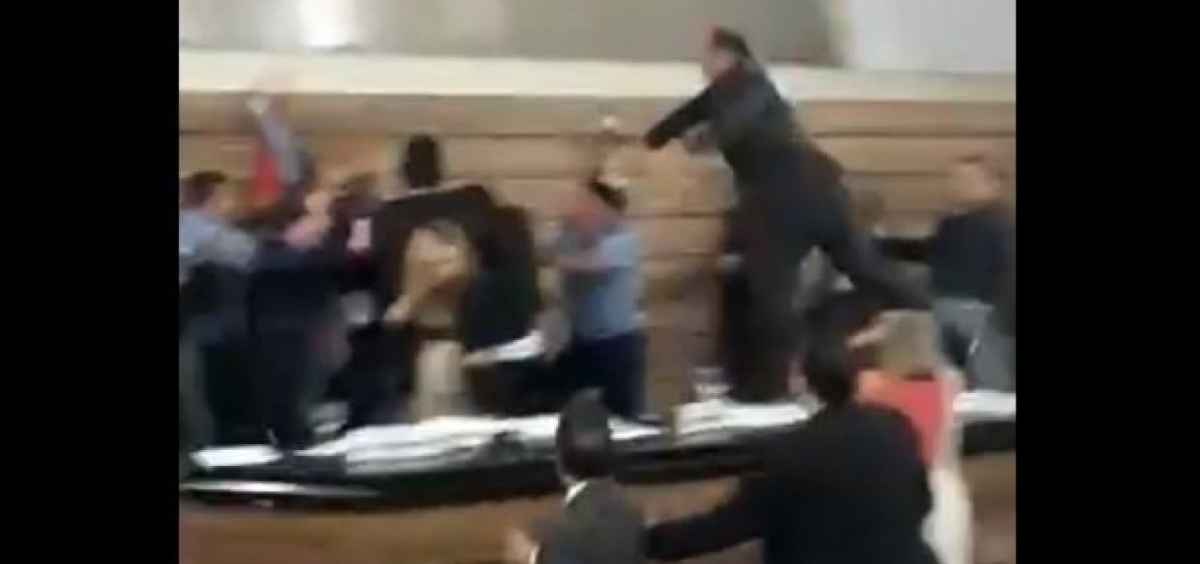 Momento em que um homem sobe na mesa diretora da Câmara e profere vários socos contra o grupo que também discutia