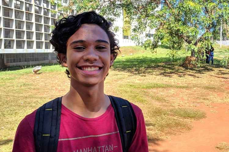 Rapaz vestindo camisa vermelha e com mochila. Ele está sorrindo