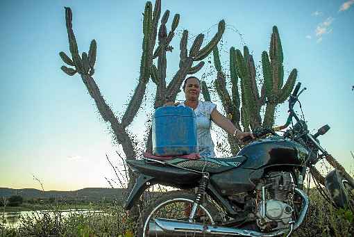 Marilene usa a moto para pegar água em um açude duas vezes por dia: o dinheiro é obtido com a Bolsa Família e a pequena roça