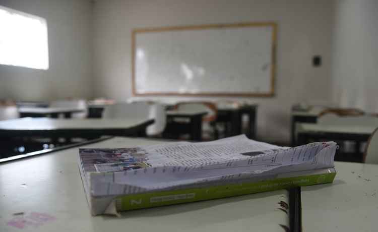 sala de aula com mesa escolar com livro, ao fundo está o quadro em branco