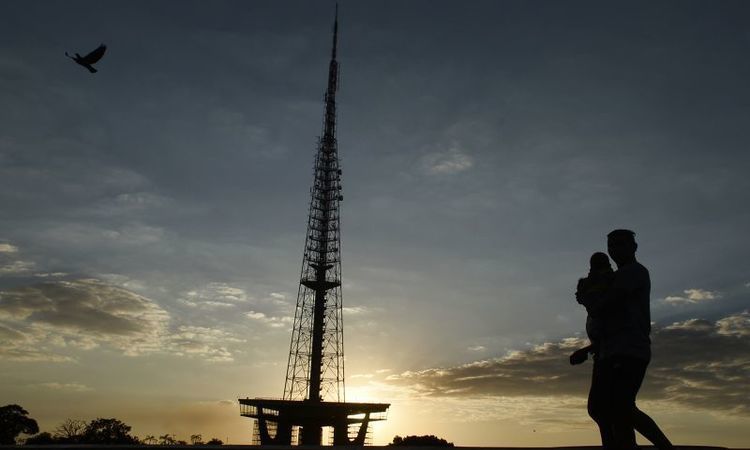 Pessoa com criança de colo andando em frente à Torre de TV