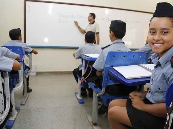 alunos têm aula fardados e estudante sorri