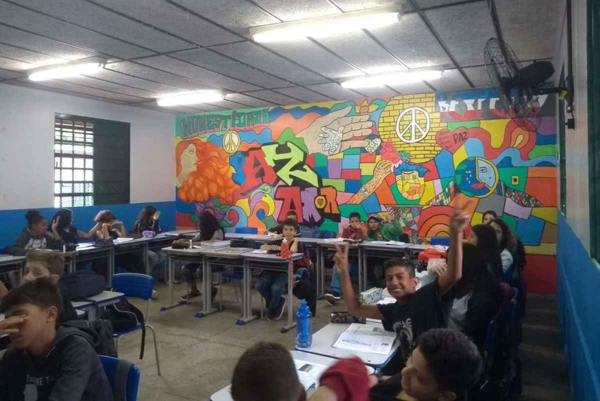 alunos assistem aula. Ao fundo tem uma parede com um grafite