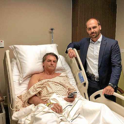 Bolsonaro com o filho Eduardo, que exibe arma na cintura: presidente quer trabalhar do hospital