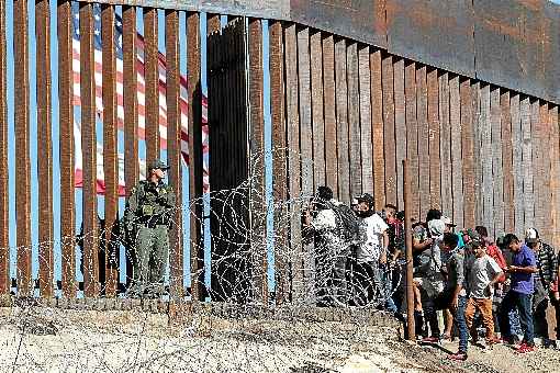 Migrantes da América Central diante do muro que separa México e EUA