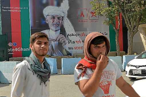 Jovens afegãos caminham em frente a outdoor de campanha de Ashraf Ghani, que tenta a reeleição