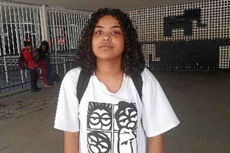 Menina negra, de cabelo enrolado, com mochila e camiseta branca