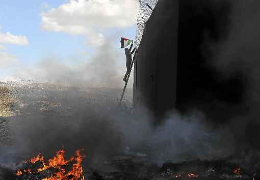 Palestino usa escada para fixar bandeira no alto do muro que separa a CisjordÃ¢nia de Israel, no vilarejo de BÃ­lin