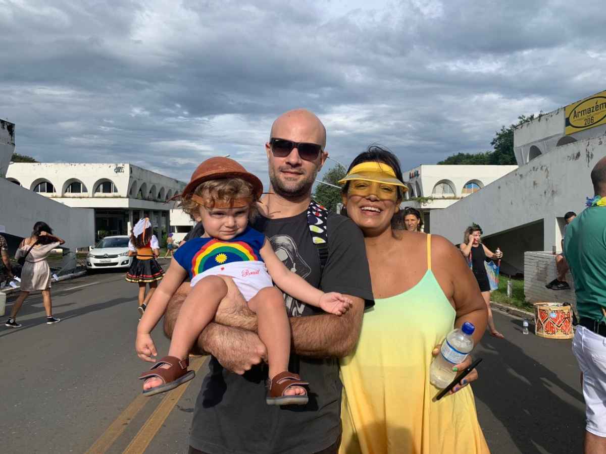 Casal posa para foto, segurando bebê no colo; bebê usa chapéu de cangaceiro e roupa com bandeira de Pernambuco