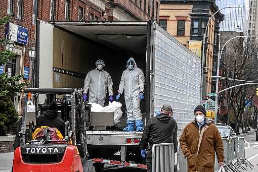 Vestidos com macacÃµes e com equipamentos de proteÃ§Ã£o, mÃ©dicos retiram corpo de empilhadeira e o colocam em caminhÃ£o frigorÃ­fico, em Nova York