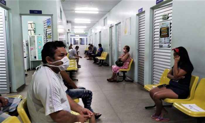 Pessoas sentadas em cadeiras no corredor de um hospital.