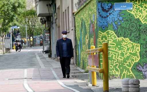 Um iraniano vestindo uma mÃ¡scara protetora passa por grafites em uma rua lateral da capital TeerÃ£ em 13 de abril de 2020 durante a pandemia de coronavÃ­rus COVID-19.