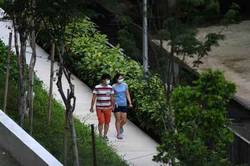 Um casal usando mÃ¡scara facial como medida preventiva contra a propagaÃ§Ã£o do coronavÃ­rus Covid-19 caminha pelo parque do bairro em Singapura.