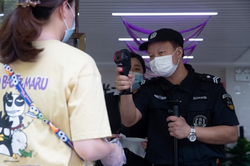 Um guarda de seguranÃ§a verifica a temperatura corporal de uma mulher em Wuhan, na provÃ­ncia central de Hubei, na China, em 11 de maio de 2020.