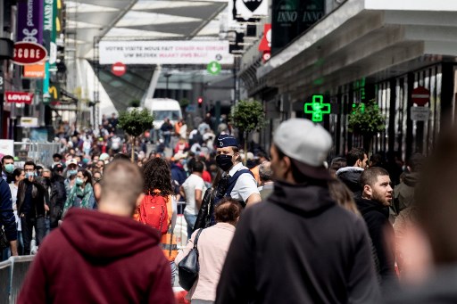 Um policial belga usando uma mÃ¡scara facial patrulha enquanto as pessoas andam na rua comercial Rue Neuve - Nieuwstraat, no centro de Bruxelas, em 16 de maio de 2020