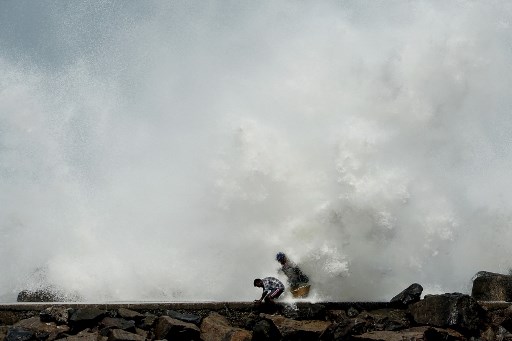 Homens passam quando as ondas atingem o quebra-mar no porto de pesca de Kasimedu, em Chennai, em 19 de maio de 2020, enquanto o ciclone Amphan se aproxima da costa leste da Ãndia.