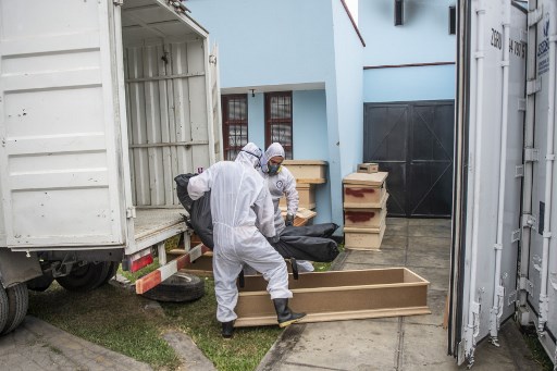 Trabalhadores carregam uma sacola com o corpo de uma vÃ­tima de covid-19 de um contÃªiner refrigerado antes de sua cremaÃ§Ã£o no crematÃ³rio El Angel, em Lima, em 21 de maio de 2020.