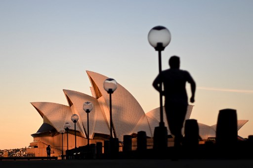 Os tons do pÃ´r do sol caem no famoso Sydney Opera House quando um homem corre no Circular Quay, geralmente lotado de turistas, em Sydney, em 16 de junho de 2020.