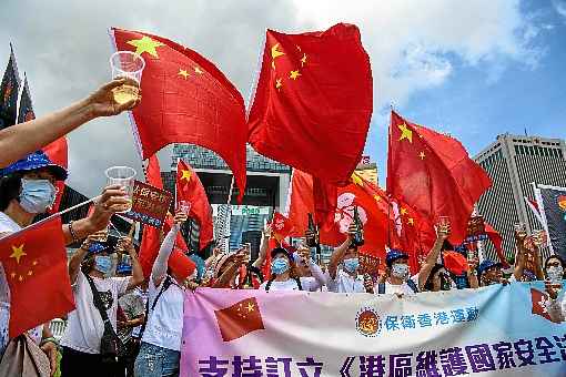 Com bandeiras e champanhe, manifestantes prÃ³-China celebram, perto do QG do governo de Hong Kong, a entrada em vigor da nova legislaÃ§Ã£o